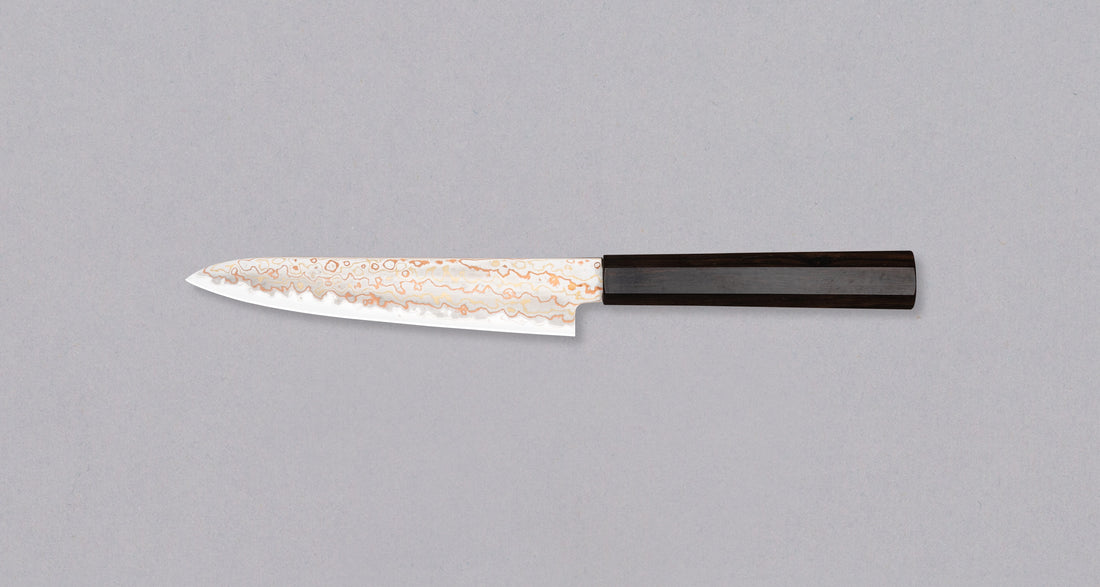 Hayabusa Petty Aogami #2 Rainbow Damascus 150 mm je zadivljujući kolekcionarski predmet, izrađen od Aogami #2 čelika, savršeno zadržava svoju oštrinu, a istovremeno ga je lako oštriti. Krasi ga jedinstveni damast uzorak s blagim mat odsjajem, koji je majstorski postignut pažljivim nanošenjem slojeva bakra i mesinga.