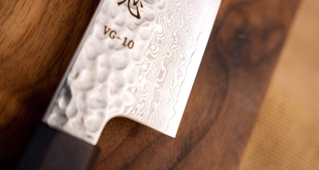 Detalj Hayabusa Gyuto VG-10 Tsuchime Damascus Ebony 210 mm koji prikazuje složeni Tsuchime završetak i elegantan damask uzorak, ističući izradu noža i kvalitetu čelika.