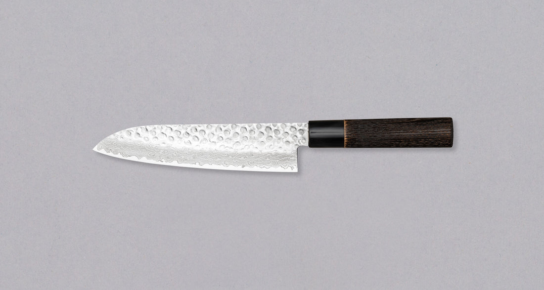 Kawamura Santoku Damascus svestrani je japanski kuhinjski nož. Jezgra je izrađena od čelika AUS-10 i obavijena u slojeve damaščanskog čelika. Gornji dio oštrice krase otisci čekića. Tradicionalna japanska drška izrađena je od paljenog drva kestena s prstenom od bivoljeg roga.