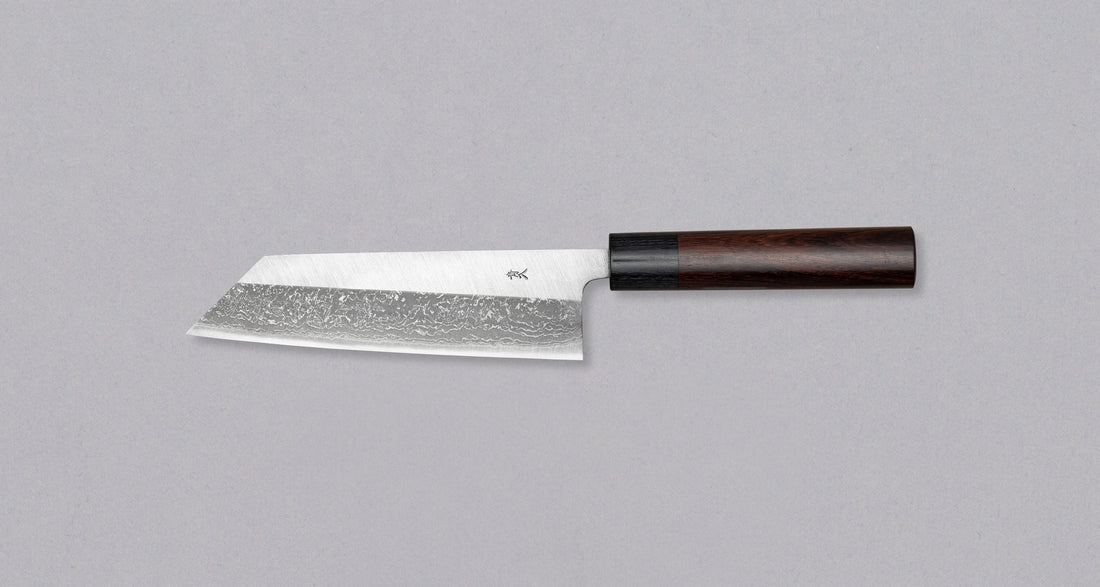 Muneishi Bunka Aogami #2 Damascus 165 mm svestrani je japanski kuhinjski nož namijenjen za pripremu mesa, ribe i povrća. Ovaj nož se drži tradicije, ali je i nadgrađuje: Oblik bunka, visokougljični čelik Aogami #2, udobna ovalna drška od palisandera. Prijelaz s migaki uzorka na magličast damast uzorak daje dašak elegancije.
