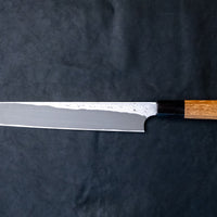 Nigara Kurozome Kiritsuke Yanagiba Aogami #2 Damascus 270 mm tradicionalni je japanski nož koji se koristi za pripremu ribe, posebno za sašimi i nigiri suši. Duljina noža omogućuje korisniku rezanje ribljeg filea jednim potezom, što zajedno s jednostrano brušenom oštricom doprinosi briljantno glatkim kriškama sašimija.