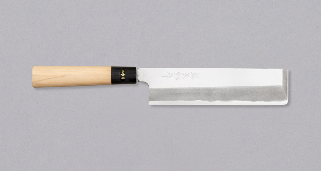 Kakugata Usuba iskovana je od Shirogami #1 čelika - jednog od najčišćih i najtradicionalnijih čelika. S ručno izrezbarenim kanjijem i tipičnom japanskom drškom od drva magnolije s prstenom od roga vodenog bivola, ovaj minimalistički nož za povrće nosi karakteristike tradicionalnih japanskih noževa koji su nam najdraži.
