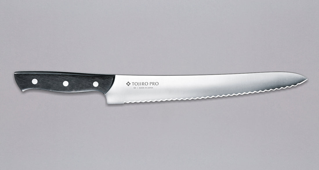 Tojiro Pankiri (nož za kruh) 270 mm_1  Ručno kovan nož za kruh Tojiro s kompaktnom drškom od crnog drveta i dugom oštricom (270 mm) nezamjenjiv je alat za profesionalne kuhare ili strastvene kuhare kod kuće. Oštrica je izrađena od molibden vanadijevog čelika s 57–59 HRC i je neosjetljiva na vanjske faktore i jako je oštra.