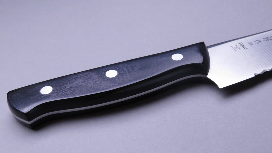 Tojiro Pankiri (nož za kruh) 270 mm_4  Ručno kovan nož za kruh Tojiro s kompaktnom drškom od crnog drveta i dugom oštricom (270 mm) nezamjenjiv je alat za profesionalne kuhare ili strastvene kuhare kod kuće. Oštrica je izrađena od molibden vanadijevog čelika s 57–59 HRC i je neosjetljiva na vanjske faktore i jako je oštra.
