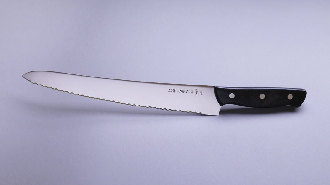 Tojiro Pankiri (nož za kruh) 270 mm_3  Ručno kovan nož za kruh Tojiro s kompaktnom drškom od crnog drveta i dugom oštricom (270 mm) nezamjenjiv je alat za profesionalne kuhare ili strastvene kuhare kod kuće. Oštrica je izrađena od molibden vanadijevog čelika s 57–59 HRC i je neosjetljiva na vanjske faktore i jako je oštra.