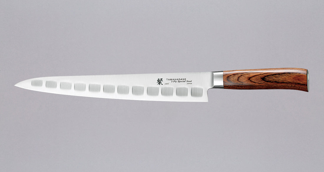 Tamahagane "SAN" Sujihiki (Fluted) 270 mm_1Slicer 270 mm: Duga i uska oštrica je prikladna za rezanje tankih komada mesa i ribe. Udubine na oštrici su estetske i korisne, jer se prilikom rezanja, zbog neravne površine, stvaraju zračni džepići koji sprječavaju lijepljenje namirnica na oštricu. Nož je zato namijenjen rezanju mesnih proizvoda i ribe npr. lososa.