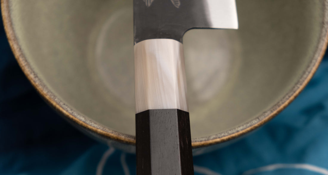 Yoshida Gyuto SUJ-2 Kuro-uchi 210 mm je ručno izrađen kuhinjski nož srednje veličine od izdržljivog SUJ-2 čelika s rustikalnim kuro-uchi završetkom, idealan za razne zadatke i s jedinstvenom gravurom koi šarana.