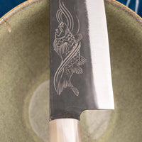 Yoshida Gyuto SUJ-2 Kuro-uchi 210 mm je ručno izrađen kuhinjski nož srednje veličine od izdržljivog SUJ-2 čelika s rustikalnim kuro-uchi završetkom, idealan za razne zadatke i s jedinstvenom gravurom koi šarana.