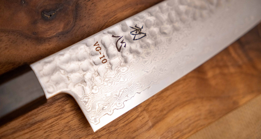 Detaljan prikaz površine i teksture noža Hayabusa Santoku VG-10 Tsuchime Damascus Ebony 180 mm, s prepoznatljivim damask uzorkom i čekićem otisnutom teksturom, koja smanjuje lijepljenje hrane na oštricu