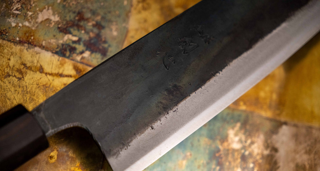 Detaljan prikaz kuro-uchi površine, kanji gravura i pete noža Kokugei Gyuto Aogami #1 Kuro-uchi Ebony 240 mm, naglašavajući ručno kovani karakter.