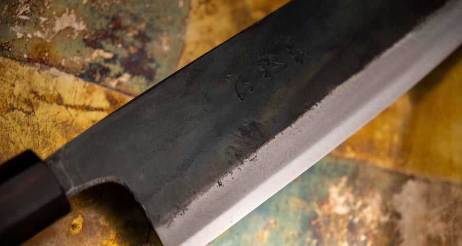 Detaljan prikaz kuro-uchi površine, kanji gravura i pete noža Kokugei Gyuto Aogami #1 Kuro-uchi Ebony 240 mm, naglašavajući ručno kovani karakter.