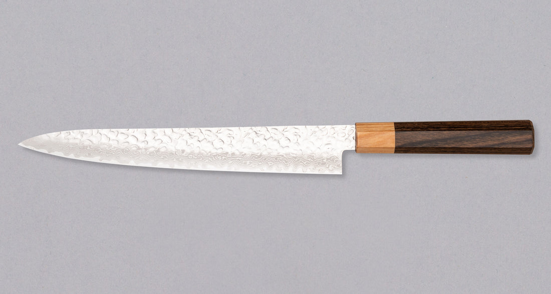 Kotetsu Sujihiki VG-10 Damascus 240 mm je nož za rezanje ribe i mesa s vidljivim otiscima čekića i klasičnom japanskom (wa-style) drškom od pakka drva. Oduševit će svakega koji cijene i estetski oblikovana kuhinjska pomagala. Duga i uska oštrica oblikovana je za rezanje ribe i mesa bez kostiju ili za filetiranje i odstranjivanje kože, jer već jednim potezom precizno odrežemo što želimo. Odabir čelika omogućuje jednostavno brušenje.