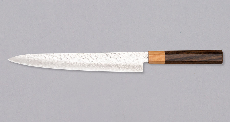 Kotetsu Sujihiki VG-10 Damascus 240 mm je nož za rezanje ribe i mesa s vidljivim otiscima čekića i klasičnom japanskom (wa-style) drškom od pakka drva. Oduševit će svakega koji cijene i estetski oblikovana kuhinjska pomagala. Duga i uska oštrica oblikovana je za rezanje ribe i mesa bez kostiju ili za filetiranje i odstranjivanje kože, jer već jednim potezom precizno odrežemo što želimo. Odabir čelika omogućuje jednostavno brušenje.