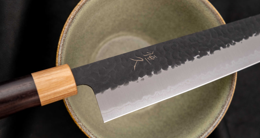 Tsunehisa Kiritsuke AS Kuro-uchi 240 mm je odličan ručno kovan nož sa crnom Kuro-uchi zaštitnom patinom i tragovima čekića. Oblik oštrice će odgovarati svima koji traže svestran nož za pripremu većih komada mesa, rezanje ribe i sjeckanje povrća. Nož je jednostavan za brušenje i održavanje.