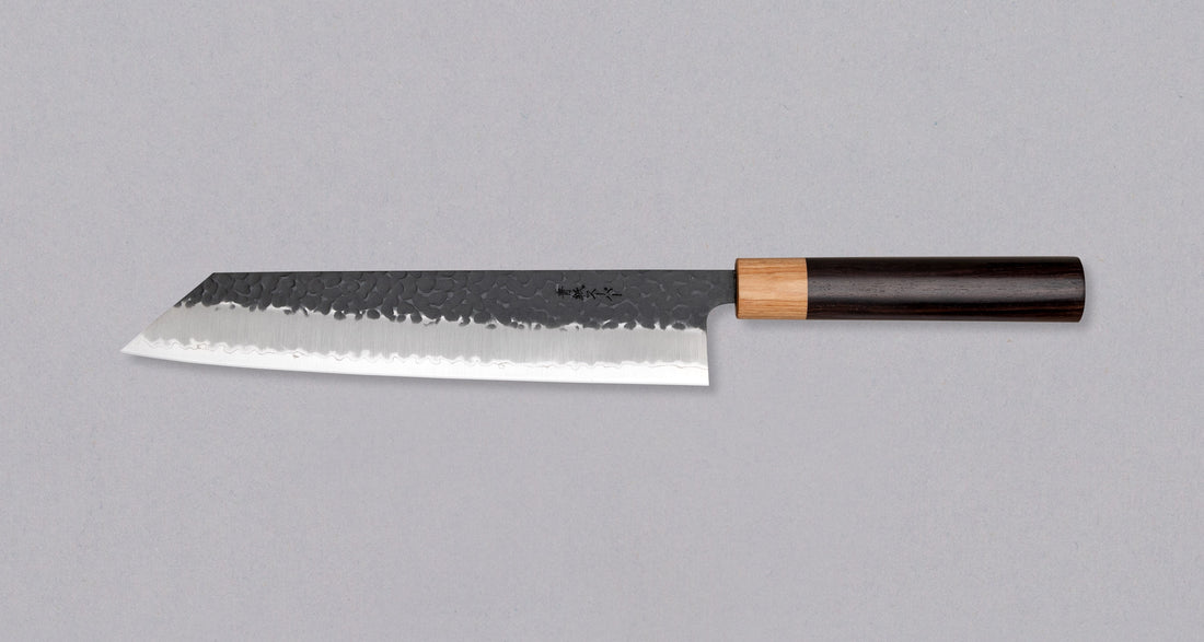 Tsunehisa Kiritsuke AS Kuro-uchi 240 mm je odličan ručno kovan nož sa crnom Kuro-uchi zaštitnom patinom i tragovima čekića. Oblik oštrice će odgovarati svima koji traže svestran nož za pripremu većih komada mesa, rezanje ribe i sjeckanje povrća. Nož je jednostavan za brušenje i održavanje.