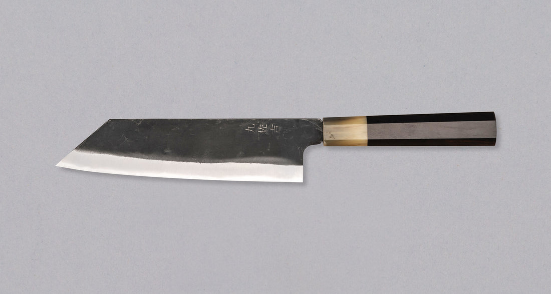 Yoshida Bunka SUJ-2 Kuro-uchi 190 mm je ručno izrađen kuhinjski nož srednje veličine od izdržljivog SUJ-2 čelika s rustikalnim kuro-uchi završetkom, idealan za razne zadatke i s jedinstvenom gravurom koi šarana.