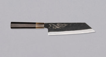 Yoshida Bunka SUJ-2 Kuro-uchi 190 mm je ručno izrađen kuhinjski nož srednje veličine od izdržljivog SUJ-2 čelika s rustikalnim kuro-uchi završetkom, idealan za razne zadatke i s jedinstvenom gravurom koi šarana.