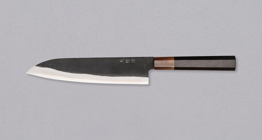 Yoshida Gyuto SUJ-2 Kuro-uchi 210 mm je ručno izrađen kuhinjski nož srednje veličine od izdržljivog SUJ-2 čelika s rustikalnim kuro-uchi završetkom, idealan za razne zadatke i s jedinstvenom gravurom koi šarana.