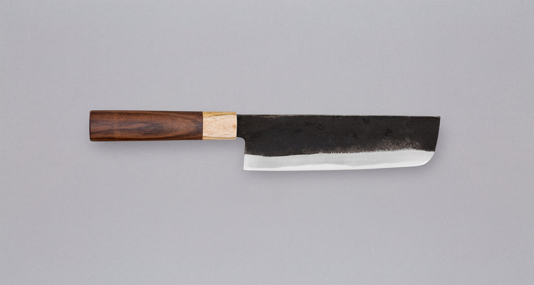 Ova oštrica Yoshida Nakiri Kyusyu SUJ-2 Kuro-uchi 165 mm [Rosewood-Cedar] iz kovačnice Yoshida Hamono ima drško od palisandra i drva cedrovine. Oštricu možete nabaviti također bez drške. Oštrica je kovana od Suj-2 čelika, tvrdoće 64 HRC, jednostavna za brušenje. Ima razvijenu tamnu patinu koja štiti oštricu.