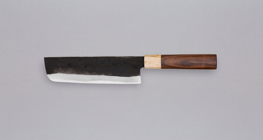 Ova oštrica Yoshida Nakiri Kyusyu SUJ-2 Kuro-uchi 165 mm [Rosewood-Cedar] iz kovačnice Yoshida Hamono ima drško od palisandra i drva cedrovine. Oštricu možete nabaviti također bez drške. Oštrica je kovana od Suj-2 čelika, tvrdoće 64 HRC, jednostavna za brušenje. Ima razvijenu tamnu patinu koja štiti oštricu.